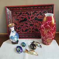 Full view of all items in the lot including the red lacquer tray, two vases, and five cloisonne ornaments on a white cloth.