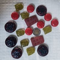 Overview showing varied vintage beads in red cinnabar, black/red floral, green carved, and maroon rectangular etched beads with twoonie for size comparison.