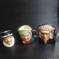 Wide angle showing all three Toby jugs together on black surface, displaying front faces and handles.