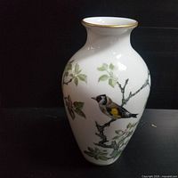 Full view of white porcelain vase with painted woodland bird and branch design, gold rim on neck.