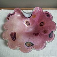 Top-down view of the pink Murano glass dish with colorful embedded millefiori patterns and scalloped edge