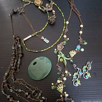 Photo showing multiple green-themed jewelry pieces including necklaces with beads, charms, and a green decorative stone.