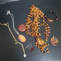 Photo showing a collection of vintage and handmade jewellery including necklaces, pendants, earrings, and a bracelet on a black surface.