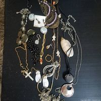 Photo showing vintage mixed jewelry laid out on black background. Includes various necklaces, earrings, rings, and pendants.