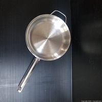 Top and side view of a new stainless steel frying pan demonstrating its size and handles.