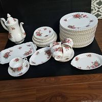 Full set displayed on floor including stacked dinner plates, smaller plates, teacups, saucers, serving trays, and a teapot all decorated with pink and red Centennial Rose floral patterns and gold trim.