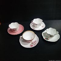 Four Shelley vintage teacups each with matching scalloped saucers, displayed on black surface in natural lighting. Various floral patterns and gold trims visible.