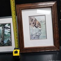 Framed print of a wolf looking at a stylized fish reflecting in water, measuring tape shows size near frame.
