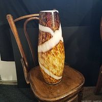 Full view of the vase showing its shape, pattern, and color, placed on a wooden chair with dark backdrop.