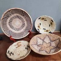 Four hand woven native baskets on table against wall, showing patterns and colors
