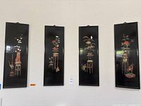 Four tall rectangular black lacquered wood panels with carved stone reliefs depicting various traditional Chinese floral, animal, and table motifs.