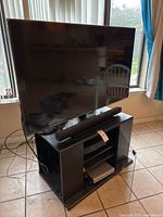 55-inch Hisense TV with attached soundbar and black TV console holding DVD and VHS players on tiled floor near windows.