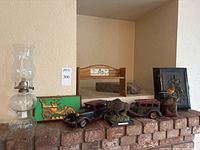 Full view of lot on brick ledge, showcasing oil lamp, brass car key hook, bison figurine, wooden cars, bird figurine, book holder, and framed art.