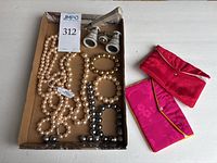 Tray with assorted beaded necklaces and bracelets, opera glasses, and two pink cloth pouches on the side