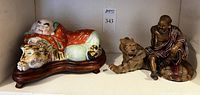 Front view of two Chinese figurines on tigers: reclining Buddha in colorful robe on left; Arhat with dark robe on right.