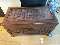 Rectangular camphor wood chest with high relief carvings on the top and front sides featuring Chinese figures and scenes.