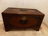 Front view of rectangular wooden chest showing carved Chinese motifs and brass lock.