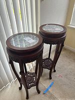 Front view of both carved rosewood plant stands with inset marble tops