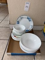Photo of assorted Corelle bowls and plates arranged on cardboard tray showing patterns and quantity.