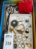 Overview of the jewelry including rings, a large flower brooch, copper bracelet, gold chain, and fabric pouches.