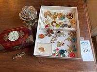 Overview of costume pins in box, with Asian style chest and metal rose bowl next to box, also small metal item in front.