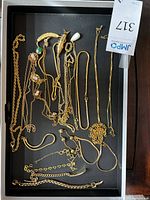 Top-down view of multiple gold tone chains and bracelets on black tray, showing intricate details of cameo and pearl pendants, varied chain styles.