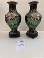 Front view of pair cloisonné vases showing chrysanthemum floral design against black background, set on wooden carved pedestals.