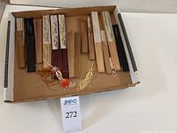 Collection of 14 wooden rib fans with tassels and varied painted designs in a cardboard box.