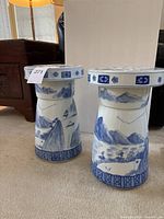 Two porcelain garden stools showing blue and white landscape side scenes including mountains, water, and trees