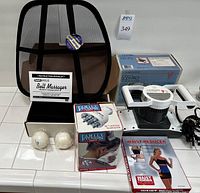 Full view of self-care products lot including Lumiscope Body Pro massager with box, Conair Body Tone massager in box, Milus belt massager with instruction manual, two white massage balls, and mesh back support.