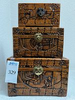 Front view of stacked three wood carved boxes showing carved floral and scenic patterns and metal latch closures