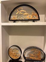 Three cork dioramas displayed together on white shelves showing varying frame shapes and detailed scenes.