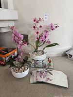 Full lot showing two faux pink orchid plants, four porcelain figurines on a glass plate, and two flat beveled mirrors placed on carpet.