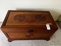 Front view of rectangular wood chest with two carved circular motifs on lid and one smaller matching motif on the front below a metal latch.