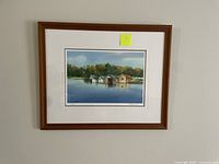 Photo of framed giclee print showing boat houses on the water with trees in background, signed and numbered.