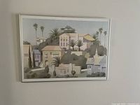 Photo of the framed art print showing a muted, stylized landscape featuring buildings and palm trees, signed by an unknown artist.