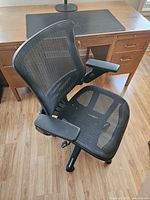 Full view of black mesh office chair showing breathable mesh seat and back with adjustable armrests and five caster wheels beneath.