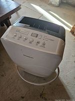 Front view of white Garrison dehumidifier showing control panel with buttons and display. Hose attached at bottom front.