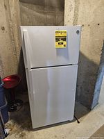 Exterior front view of closed white GE top freezer refrigerator with EnergyGuide label.