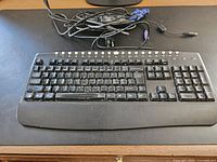 Photo shows a full black wired computer keyboard with numeric keypad and a set of assorted connection cables placed on a desk.