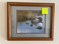 Framed artwork showing two loons on water with natural vegetation, signed by Henske.