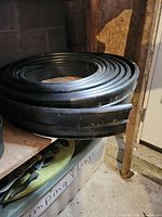 Black coiled plastic garden edging roll placed on a wooden surface near a door, showing the height measurement and material texture.