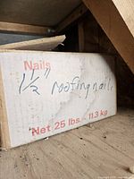 Cardboard box on a shelf labeled as containing 1.5 inch roofing nails, marked Net 25 lbs (11.3 kg), handwriting indicates roofing nails