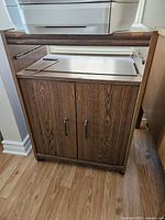 Front view of the wooden cabinet with two closed doors, showing the top surface with a printer placed on it.