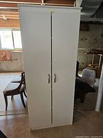 Closed white storage cupboard with two vertical doors and silver handles.