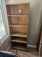 Front view of the wood shelving unit showing four adjustable shelves inside a tall, light brown wood frame.