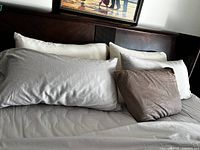 Four king pillows on grey sheet with two white protectors and two grey pillowcases, plus one brown-covered standard pillow