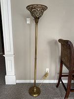 Full view of tall brass-finish torchiere floor lamp showing slim pole, weighted base, and decorative glass shade on top.