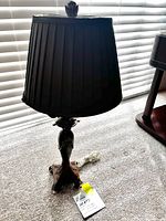 Full view of the bedside table lamp showing the black pleated fabric lampshade and ornate metal base with some visible wear on the feet.