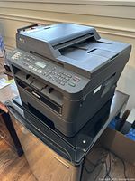 Left-angled view of Brother MFC-7860DW multifunction printer showing control panel and input/output trays.